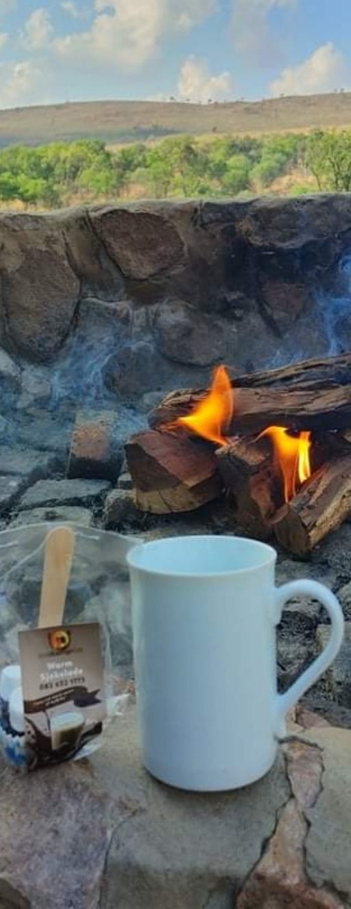 Warm Sjokolade sakkie en 'n enemmelbeker langs 'n brandende kampvuur in die bosveld